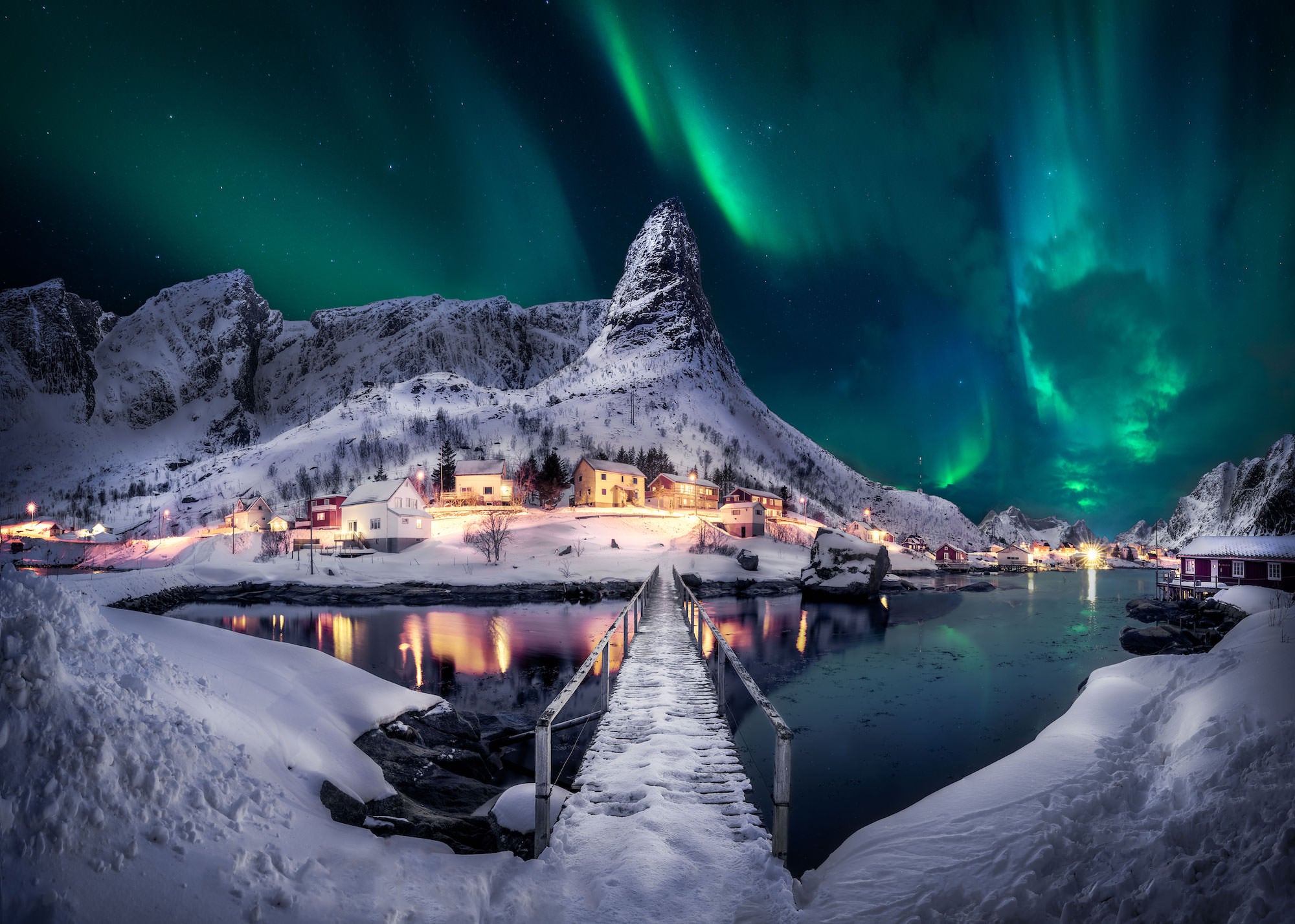 Photo at night of aurora over snowy mountain town in Norway.